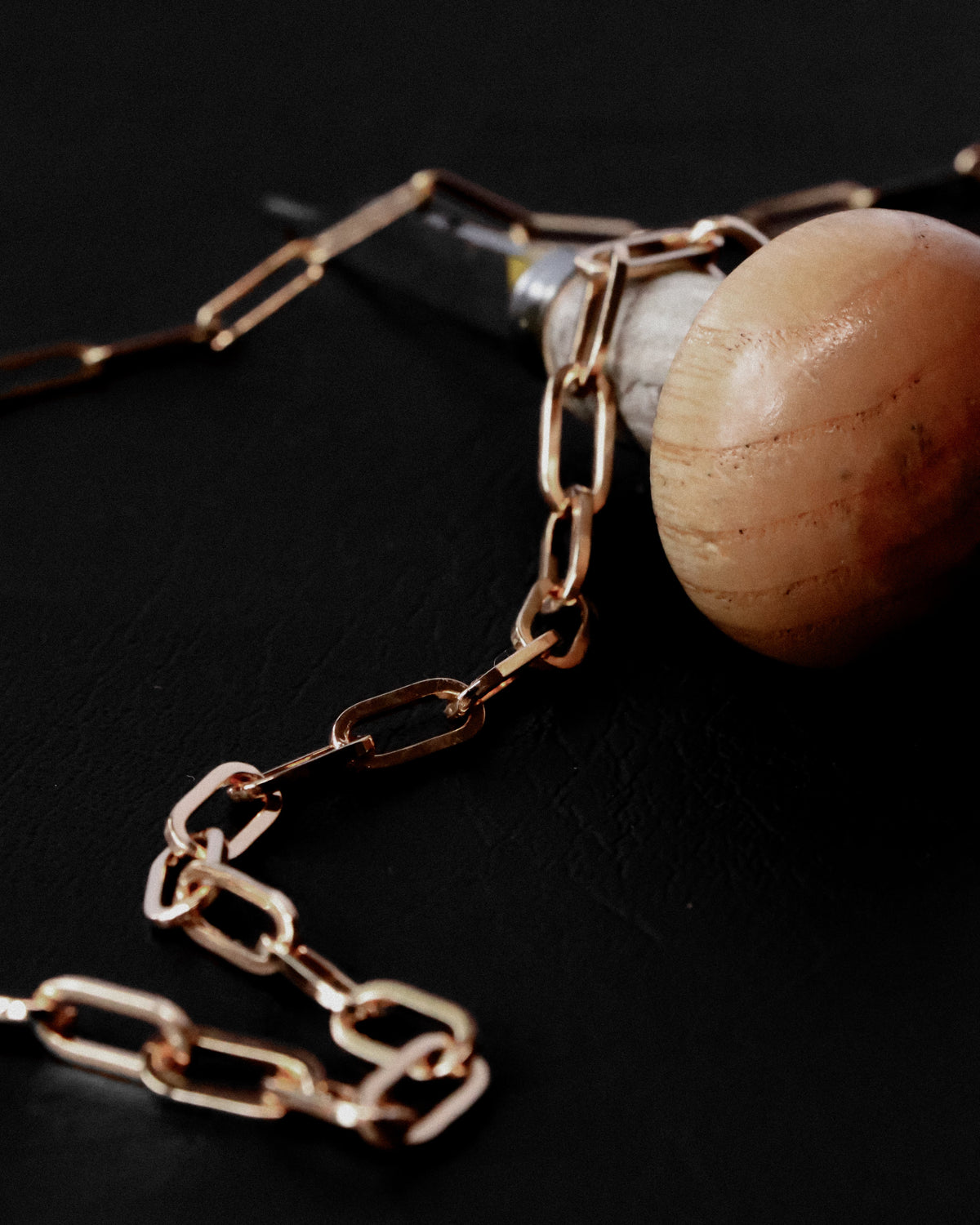 A close-up of a gold-toned chain draped over a light wood sphere on a dark black background.