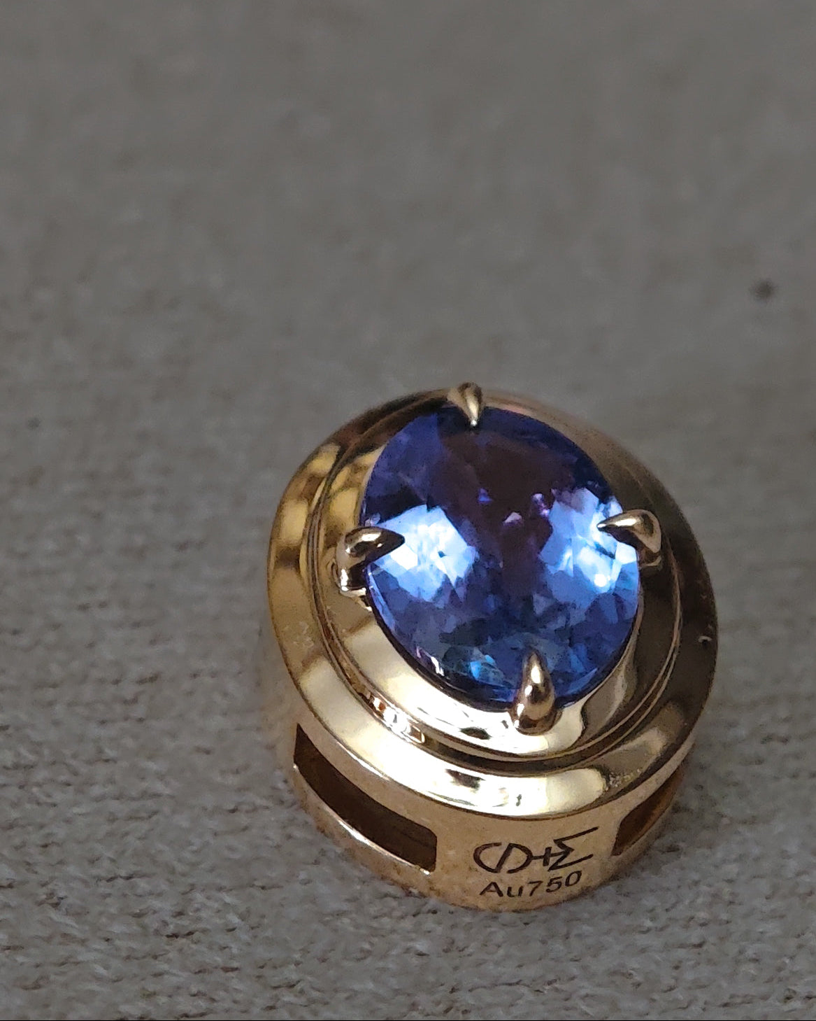 A gold ring featuring a large oval-cut tanzanite in a prong setting, resting on a textured gray surface.